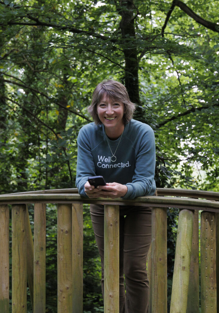 Blond woman leans on a wooden bridge, holding a phone.